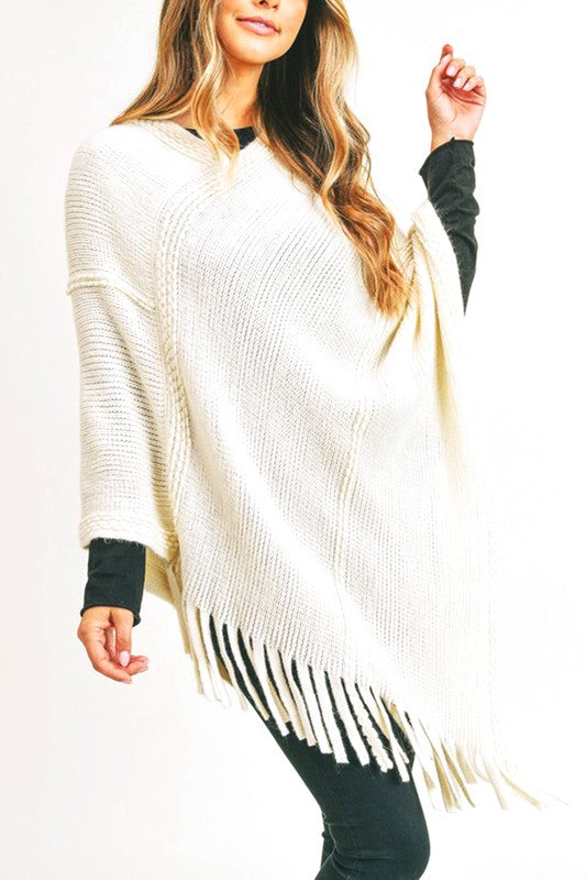 Ivory knit poncho with fringe, offering a warm and elegant layer to complement various outfits.