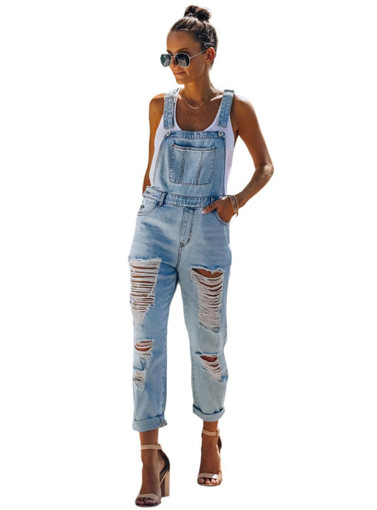 Front view of women’s washed ripped blue jean overalls styled with a white tank and nude heels.
