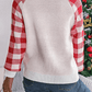 Close-up of white knit sweater with a red reindeer graphic and buffalo plaid sleeves