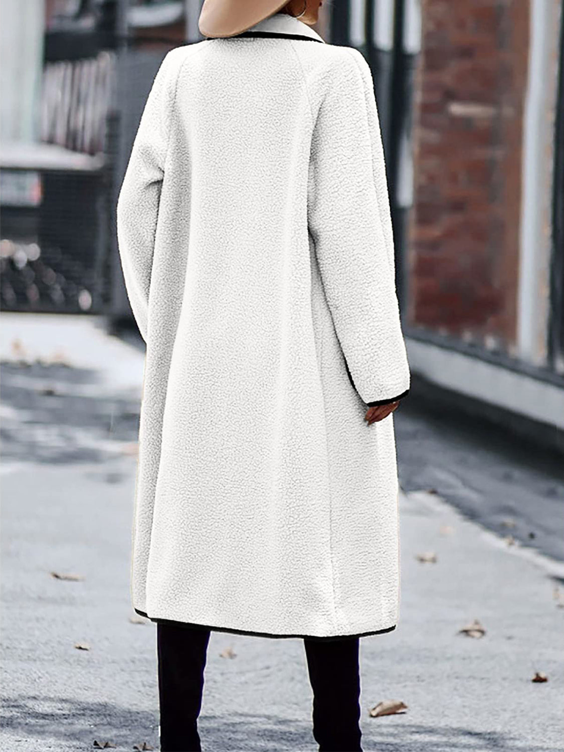 White long sherpa coat featuring oversized pockets and black trim.
