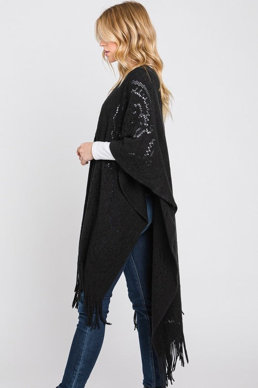 Black paisley-pattern knit poncho styled over neutral tones.
