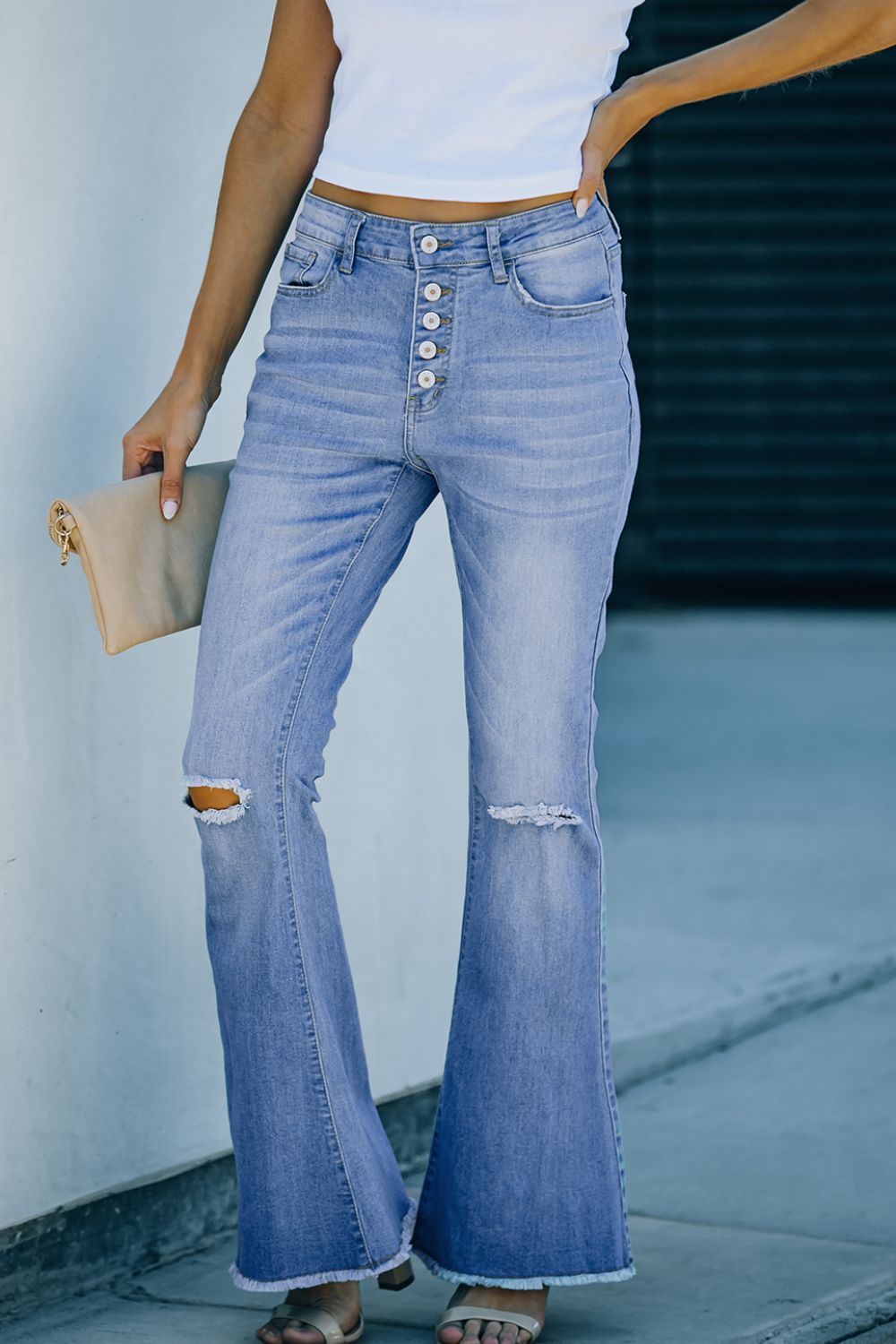 Front view of button-fly distressed raw hem flare jeans in light blue denim with knee distressing and a high waist.