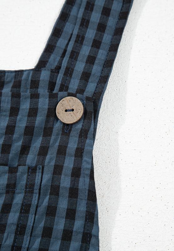 Close-up of wide strap detail and plaid pattern on black wide-leg overalls.
