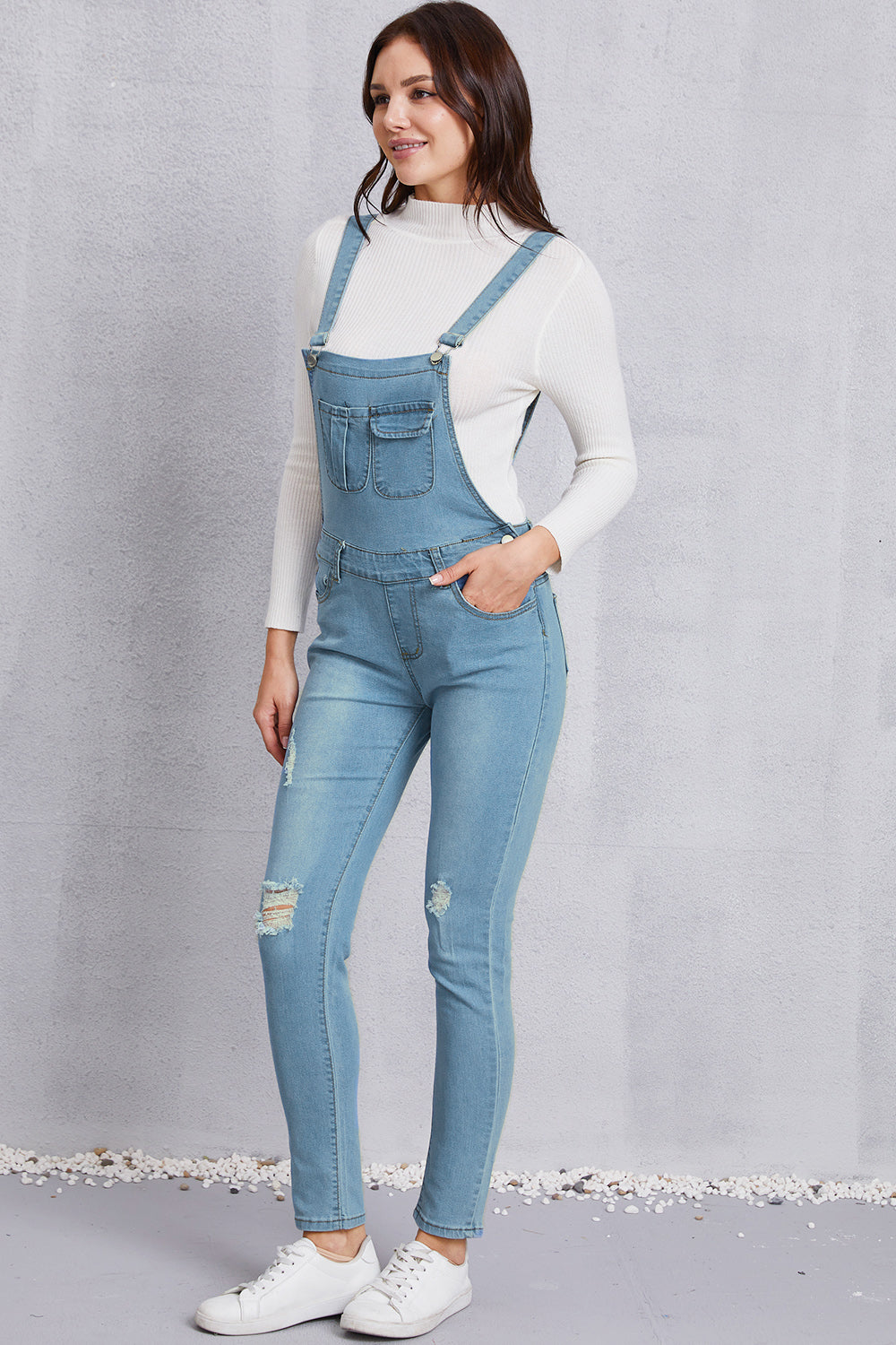 Women’s trendy washed denim overalls with mid-waist design and ripped knees.
