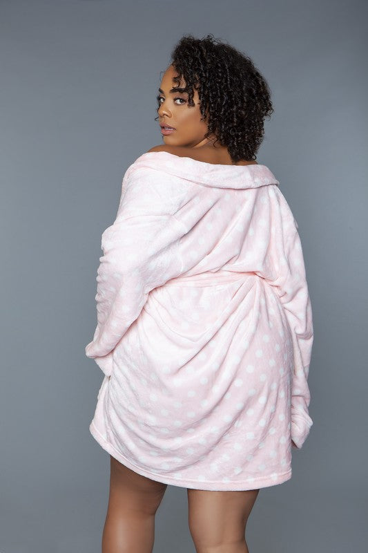 Woman lounging in a pink plush robe with polka dots, complete with a tie belt and cozy fit.
