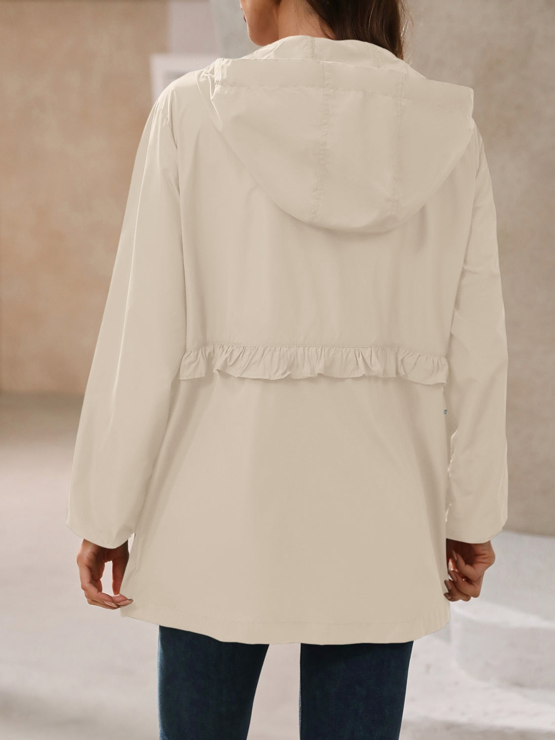 Back view of a tan womens rain jacket with a cinched waist and hood.
