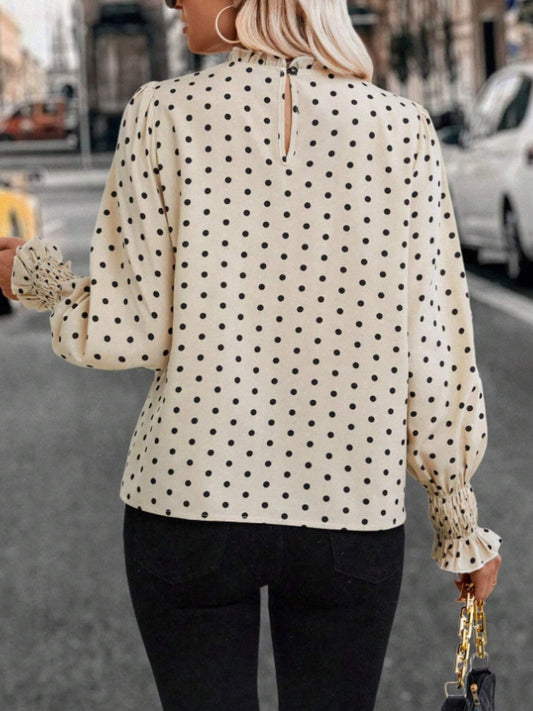 Women’s long sleeve polka dot blouse with ruffled cuffs, styled with black pants for a polished outfit.
