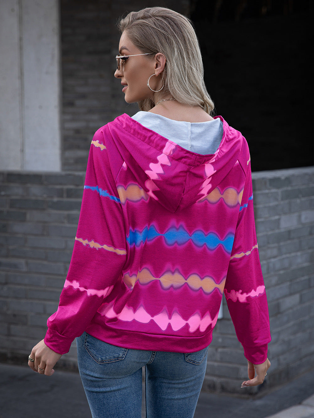 Close-up of a woman in a pink tie-dye hoodie with a relaxed fit and white drawstrings, styled for a casual day out.
