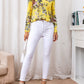 Bright yellow blouse with floral print and ruffled shoulders, styled with white jeans and a casual purse.
