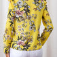 Floral V-neck blouse with ruffled shoulders in a bright yellow fabric, perfect for a casual day out.
